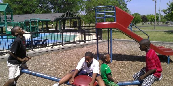 Four boys playing on a seesaw in a sunny playground.
