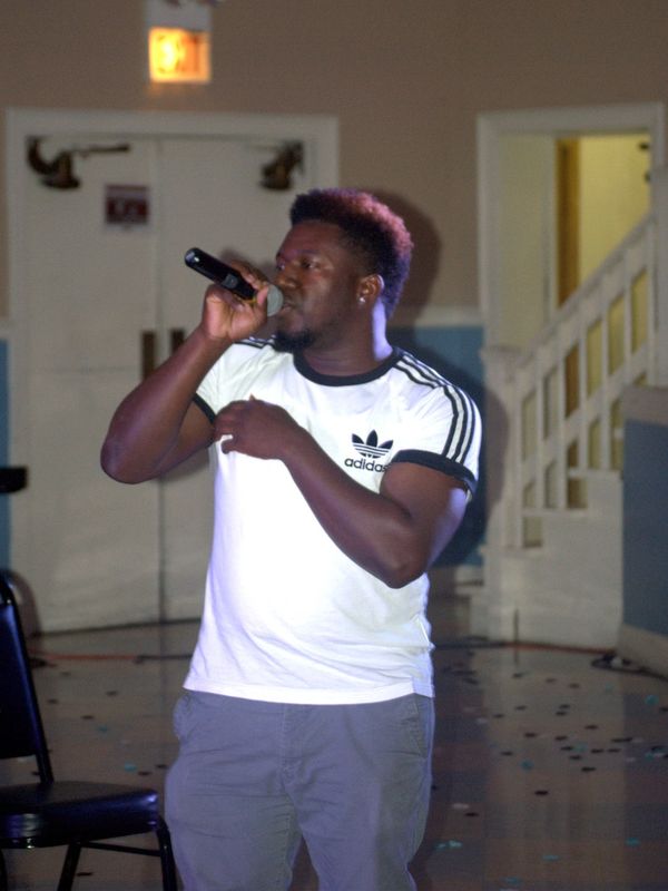 Man singing into a microphone indoors near stairs.