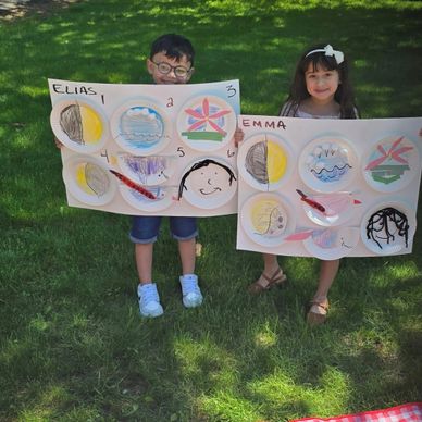 Two children proudly display their colorful art projects outdoors.