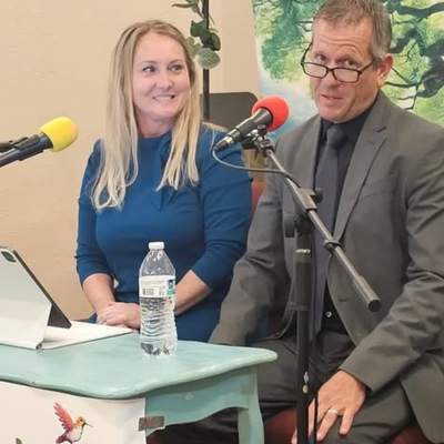 Two people speaking into microphones at a desk during a discussion or interview.