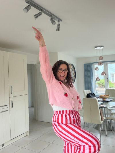 Woman joyfully poses indoors in pink and red striped outfit.