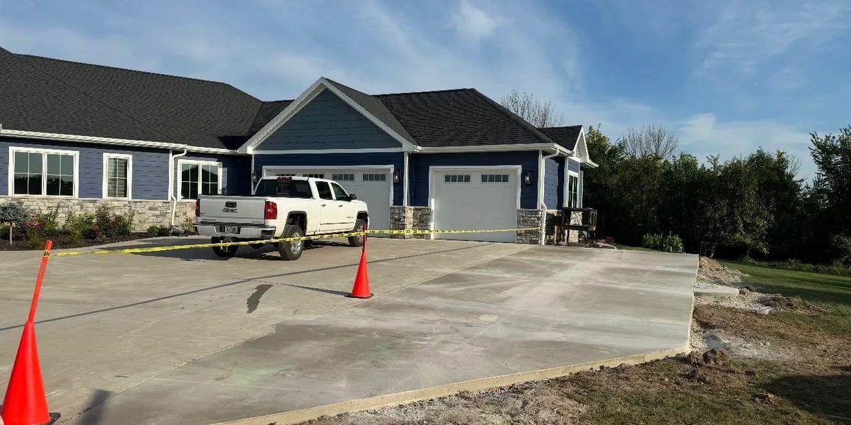 Newly poured concrete driveway in front of a house with caution tape and cones.