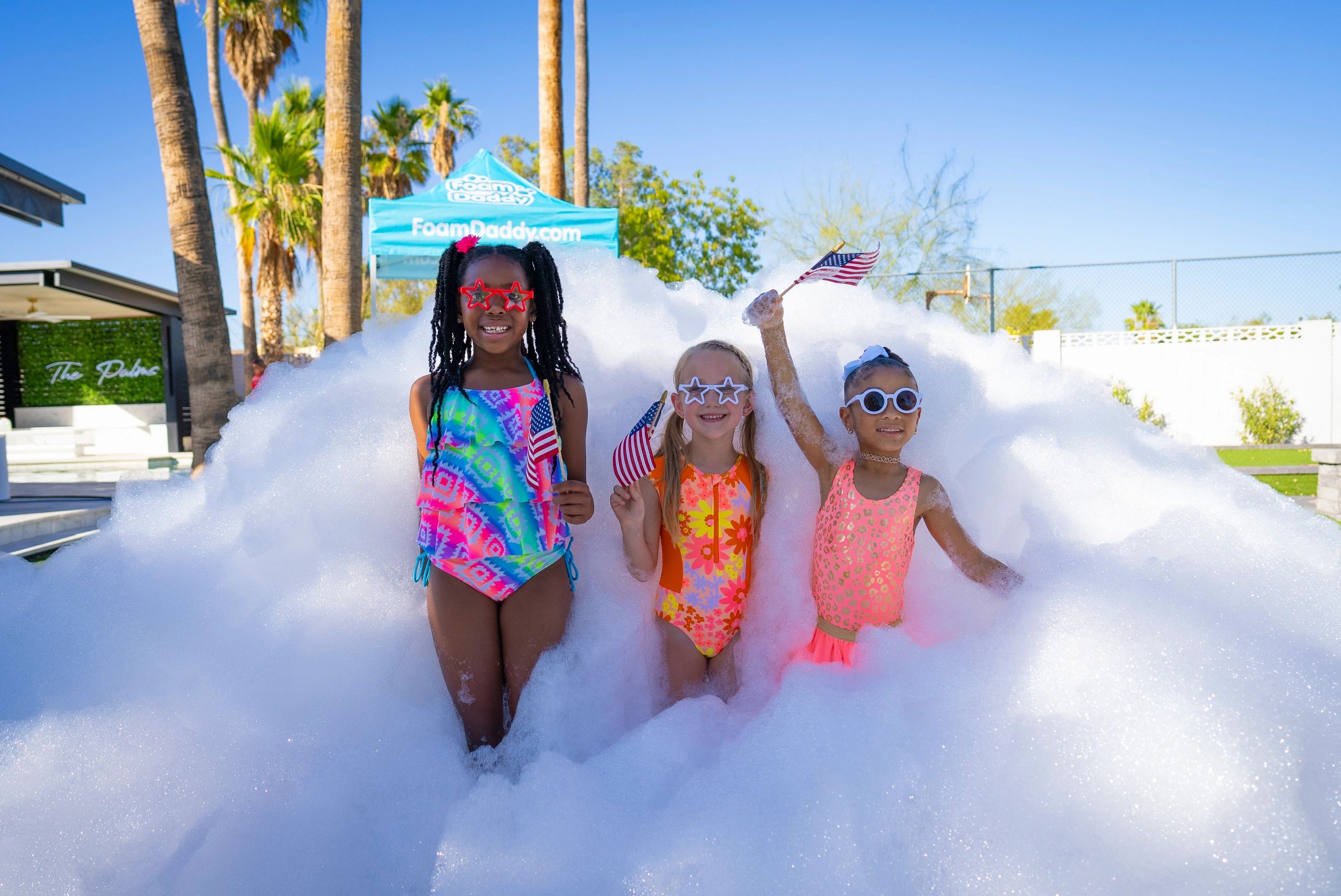 Three girls in swimsuits having fun in foam with American flags.