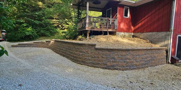 Curved retaining wall beside a red house in a garden.