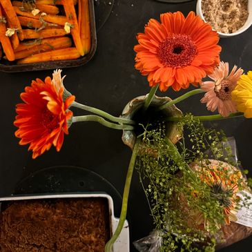 Orange and yellow flowers in a vase on a table with food dishes.