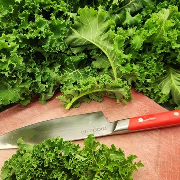 Fresh green kale leaves with a knife on a cutting board.