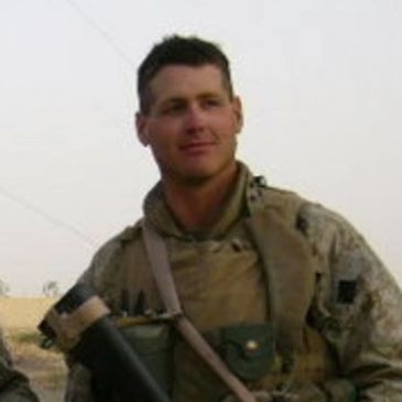 A soldier in military gear standing outdoors, holding a weapon.