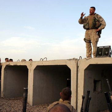 A military instructor trains soldiers standing on a concrete structure outdoors.