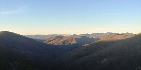 Sunlit mountain range under a clear blue sky at dusk.