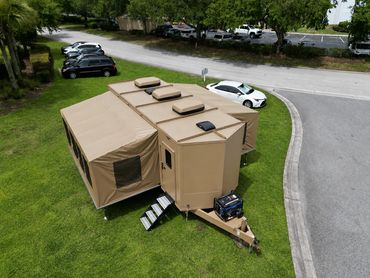 Beige expandable camping trailer with a generator parked on grass.
