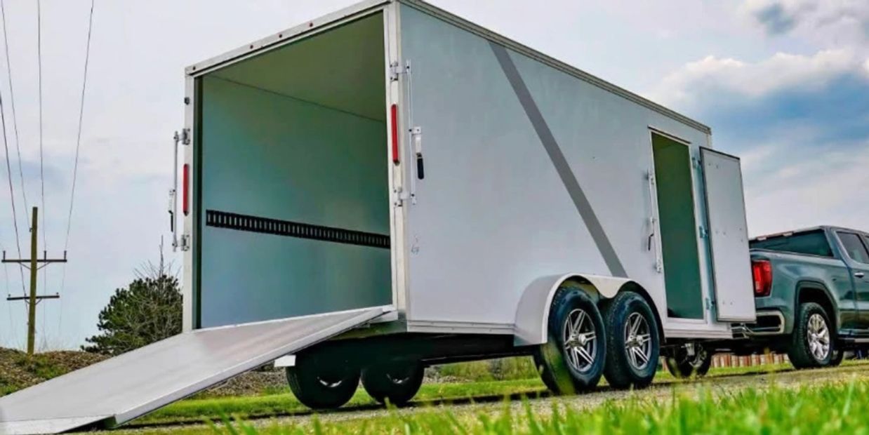 A white enclosed trailer hitched to a pickup truck with its ramp and side door open.