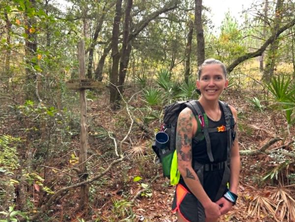 Smiling woman with tattoos hiking in a forest.