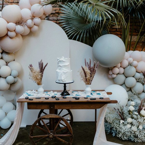 Rustic wedding cake setup with white balloons and dried floral decor.