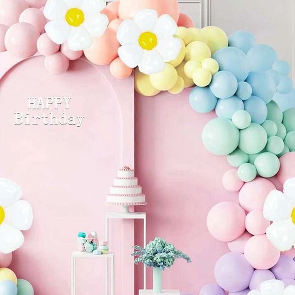Pastel balloon arch with flowers and birthday cake on pink backdrop.