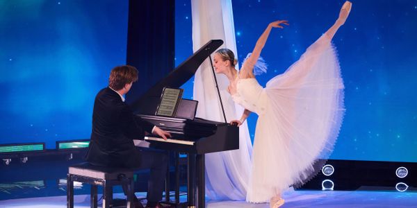 A ballerina dances gracefully beside a pianist on stage.