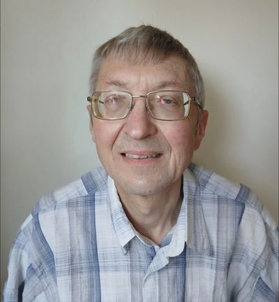 Smiling elderly man wearing glasses and a checkered shirt.