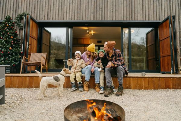 Family enjoying a campfire outside a cabin with their dog.