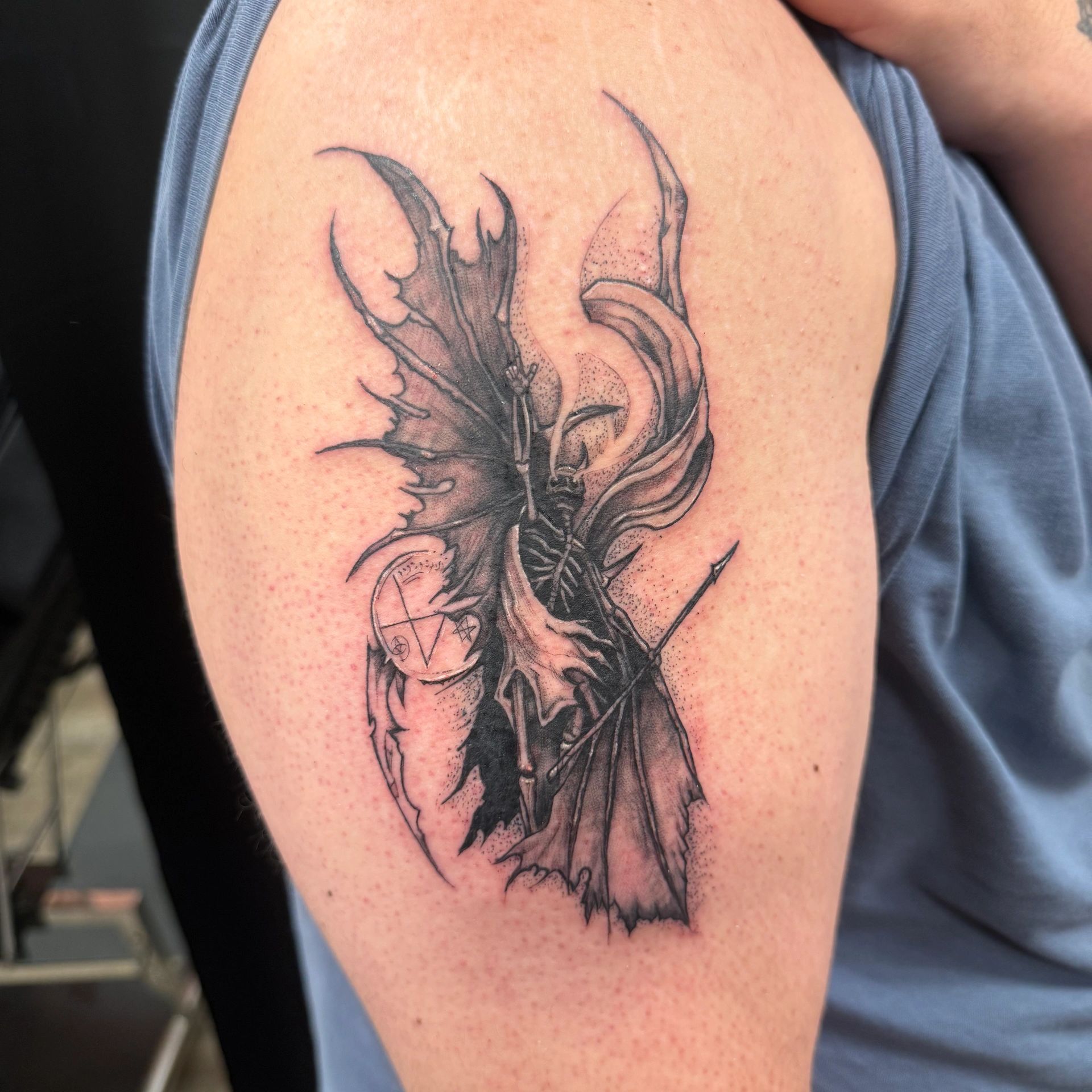 Tattoo of a skeletal figure with wings and a spear.
