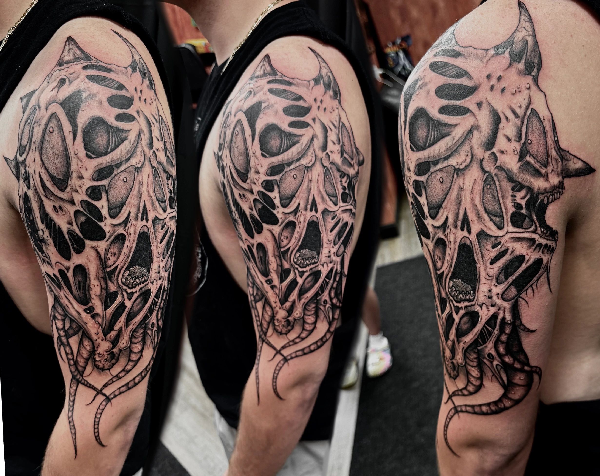 Detailed black and grey alien skull tattoo on upper arm.