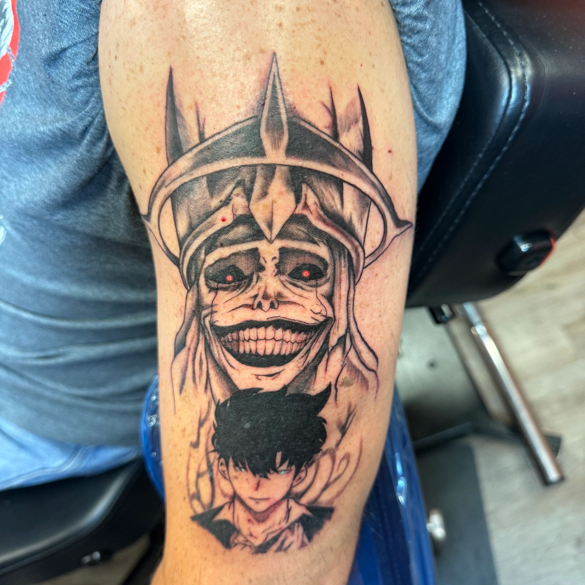 Tattoo of a sinister figure with a spiked crown and a serious young man below.