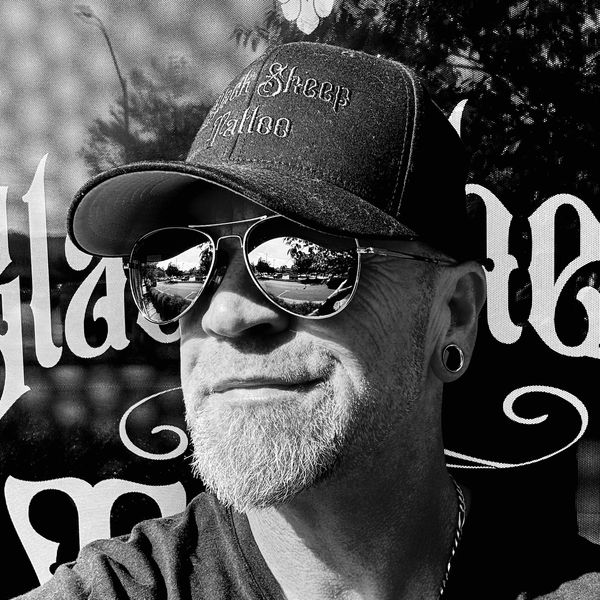 Man wearing a cap and aviator sunglasses smiling.