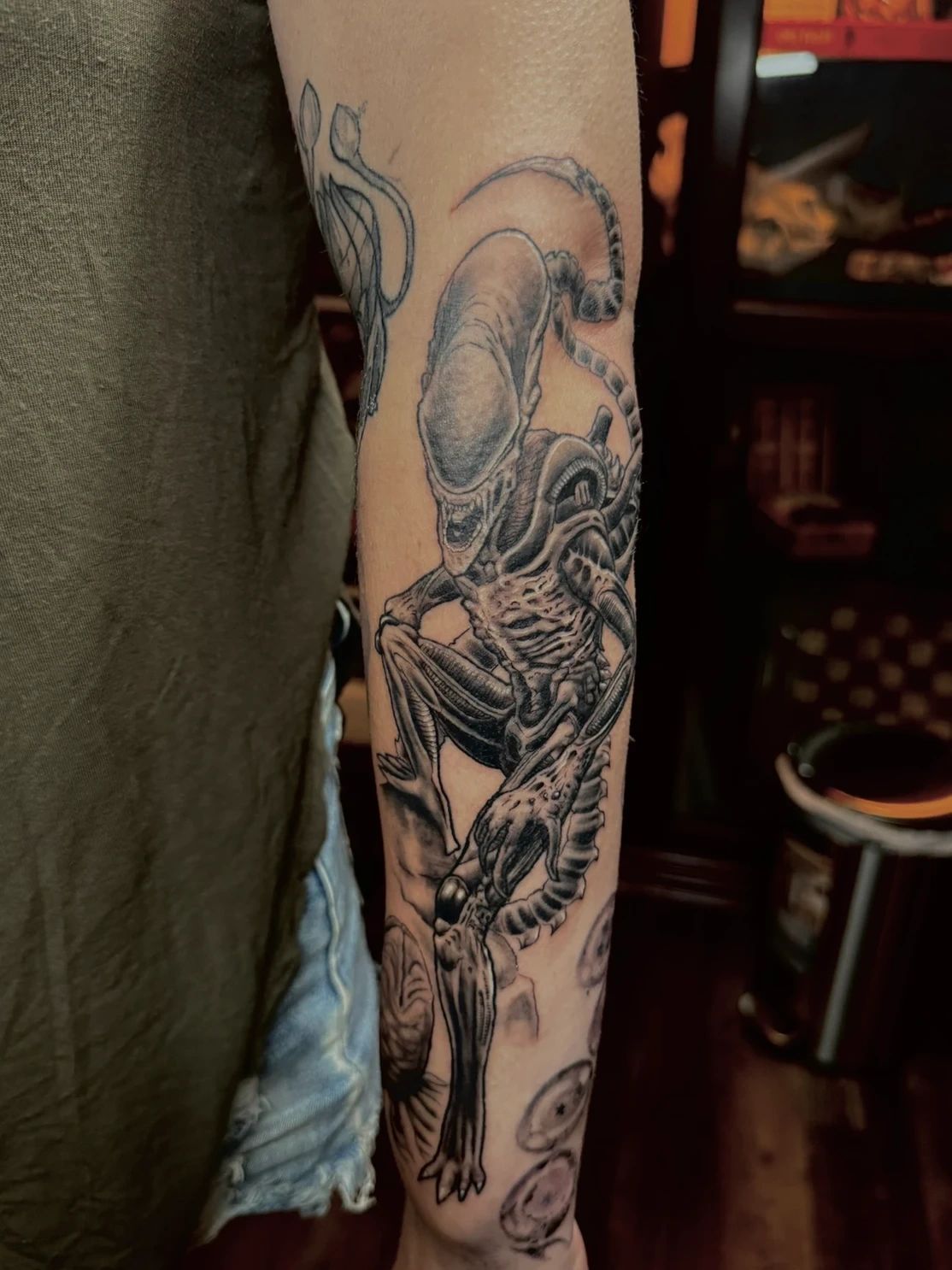 Realistic alien creature tattoo on arm.