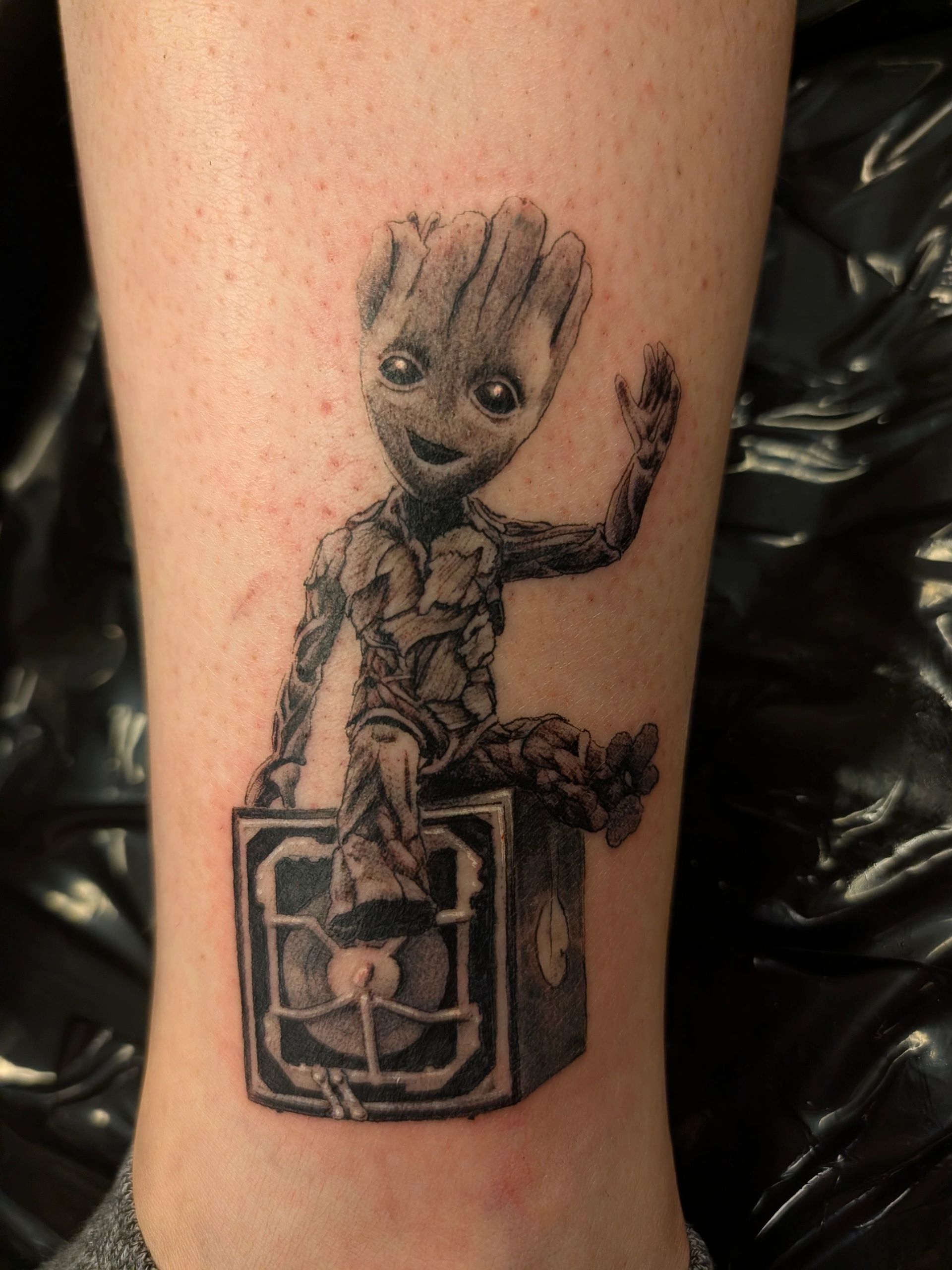 Tattoo of Baby Groot sitting on a speaker, waving.