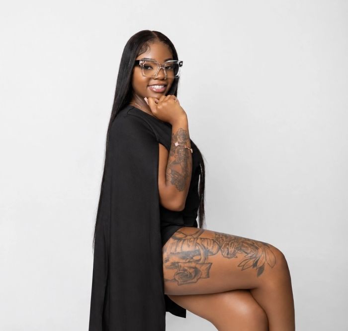 Smiling woman with tattoos and glasses, wearing black outfit.