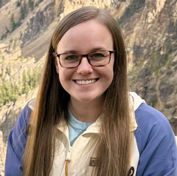 Smiling woman with glasses outdoors in a mountainous area.