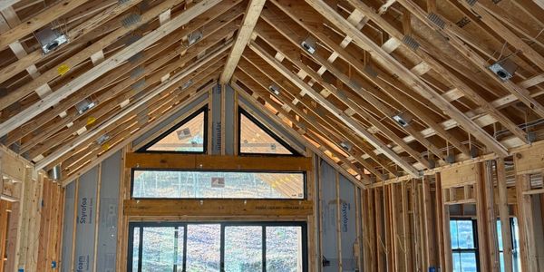 Interior of a wooden house under construction with exposed framing and a vacuum cleaner.