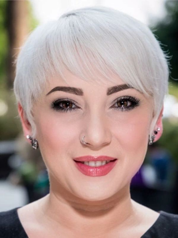 Smiling woman with short white hair and stylish makeup.