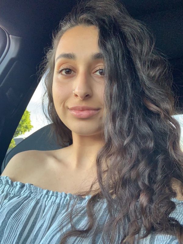 Young woman with long curly hair in a car, wearing an off-shoulder top.