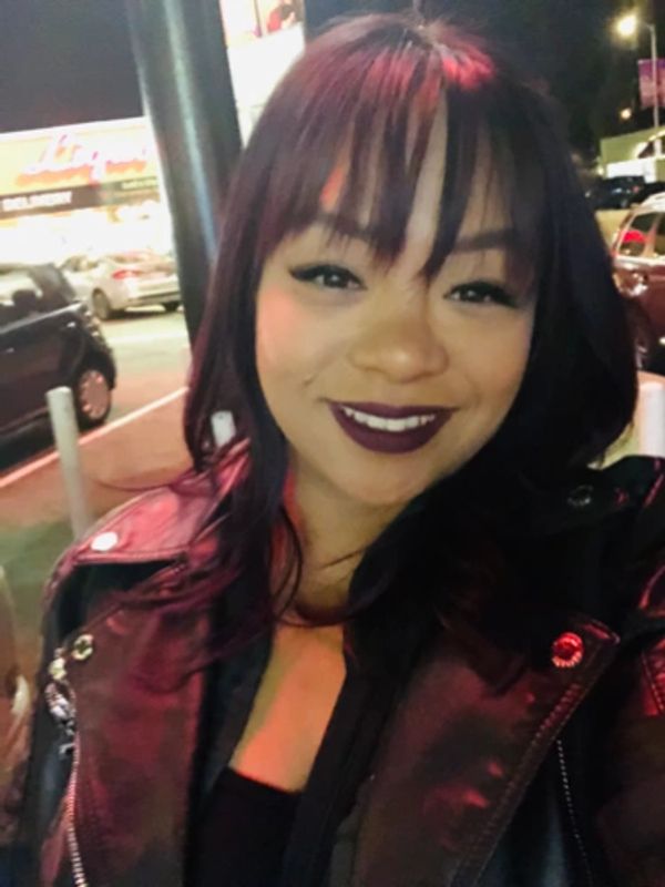 Smiling woman with dark lipstick and leather jacket in nighttime urban setting.
