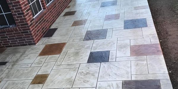 Patterned tiled walkway with various colored tiles beside a brick wall.