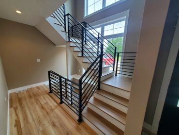 Modern staircase with black railings and wooden flooring.