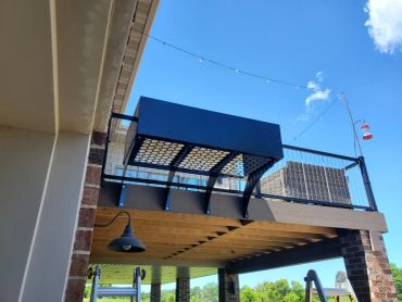 A wooden deck with a black railing and outdoor light under a clear blue sky.