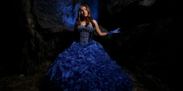 Woman in an elaborate blue gown standing in a dark cave.