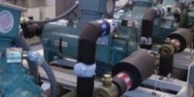 A row of industrial pumps connected with black insulated pipes.