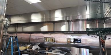A stainless steel kitchen wall with cooking equipment and a blue ladder.