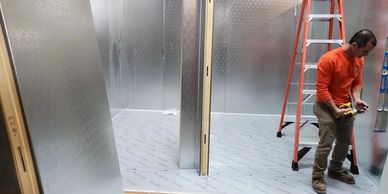 Worker assembling metal panels inside a construction area with a ladder nearby.