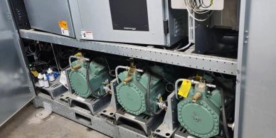 Three green industrial compressors installed in a metal frame inside a facility.