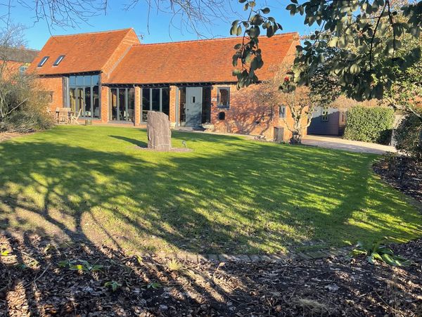 Sunny day at a charming boutique barn conversion with a large green lawn and a stone centerpiece.