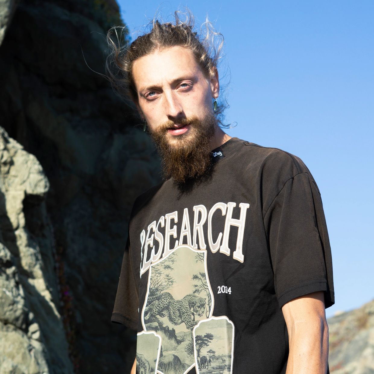 Man with a beard wearing a black 'RESEARCH' t-shirt outdoors.