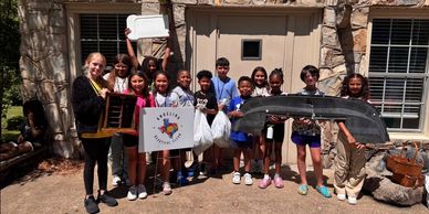 Group of kids holding various items outside a building.