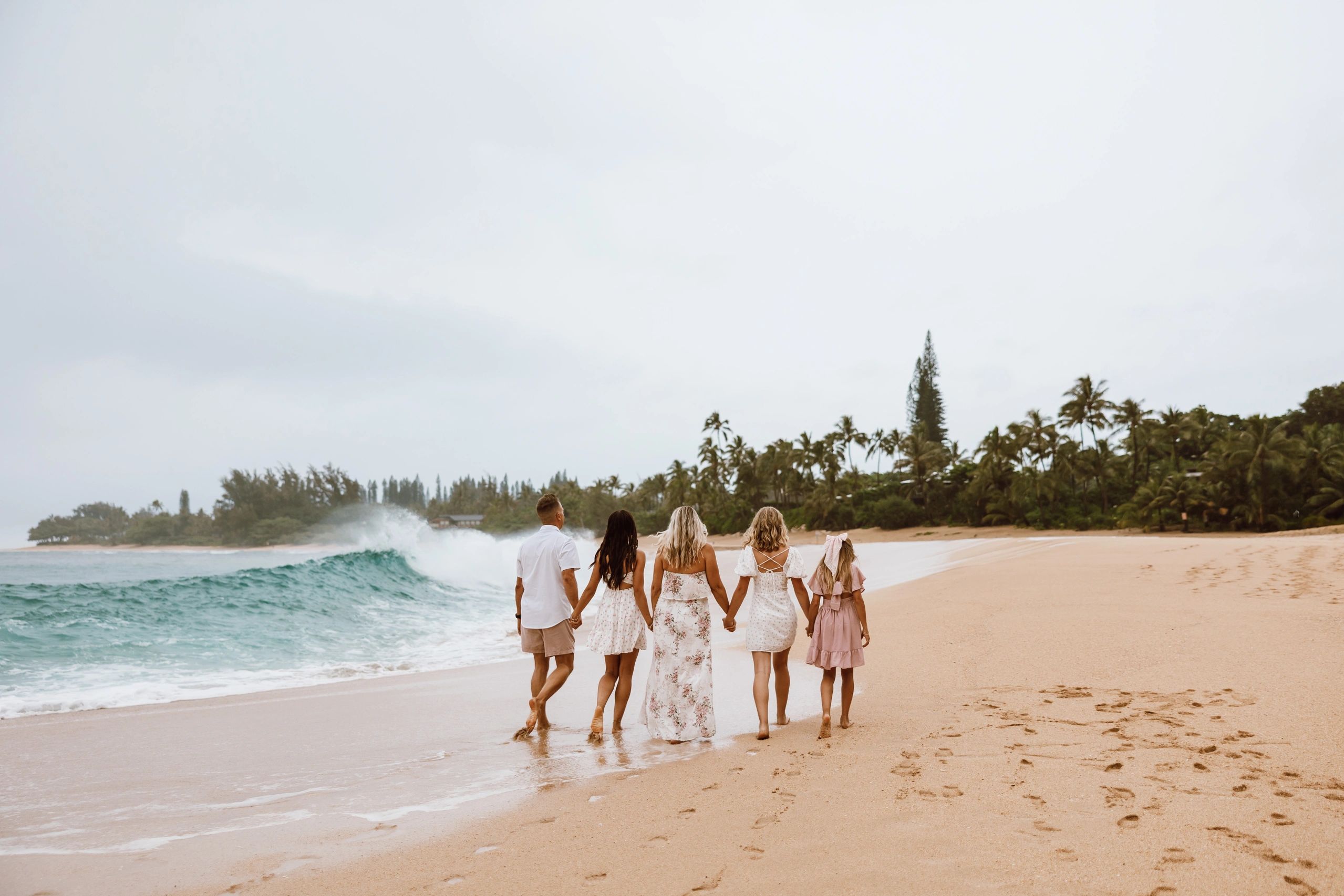 Five people holding hands and walking along a beach with waves and palm trees.