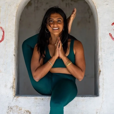 Woman in teal yoga outfit performing a complex pose in a wall niche.