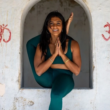 Woman performing advanced yoga pose inside an arched window frame.