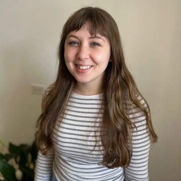 Young woman with long brown hair smiling, wearing a striped shirt.