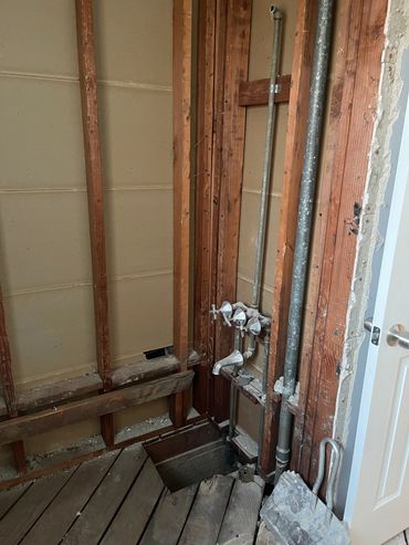 Exposed wall studs and plumbing pipes in a partially demolished room.
