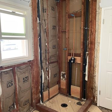 Bathroom shower area under construction with exposed wood and insulation.